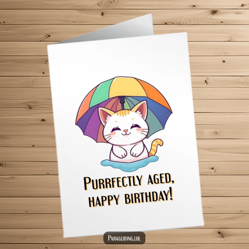 Free Printable Birthday Card: A smiling cat floats serenely beneath a vibrant rainbow umbrella, exuding calm.